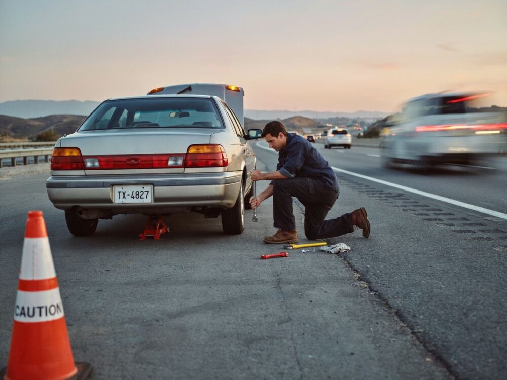 mężczyzna zmieniający koło na autostradzie